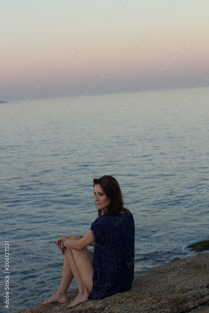 beautiful brazilian woman with brown hair sitting on rocks on the beach called arpoador city rio de janeiro