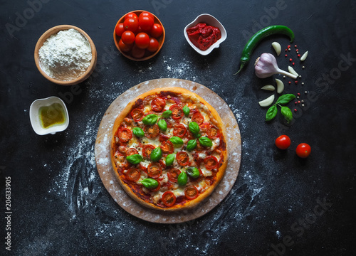 Italian pizza Margarita with cherry tomatoes and green basil on black background. 