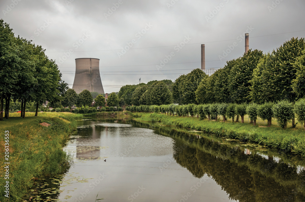 View of canal and gardens with nuclear power plant in background on cloudy day, near the village of Geertruidenberg. A small, friendly place near Aakvlaai Park and Breda. Southern Netherlands. View of canal and gardens with nuclear power plant in background on cloudy day, near the village of Geertruidenberg. A small, friendly place near Aakvlaai Park and Breda. Southern Netherlands.