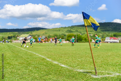 Retro corner flag on the foreground of amateur soccer field, on blurry background are football players fighting for the ball