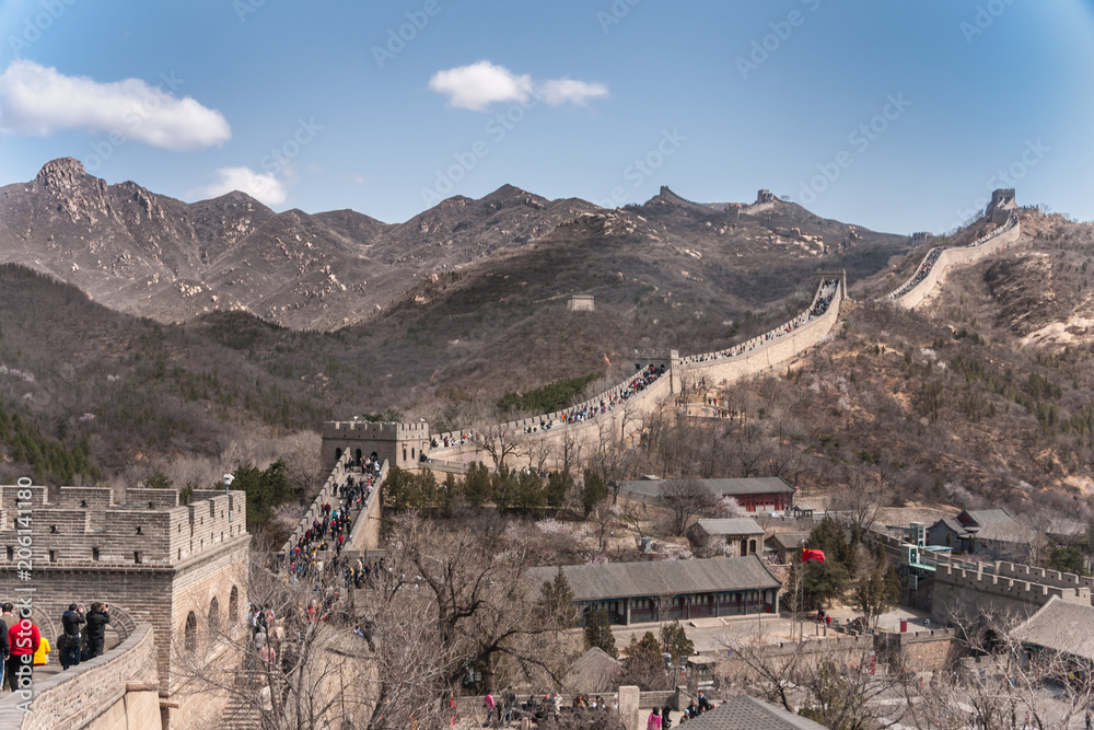 Beijing, China - April 28, 2010: Great Wall of China at Badaling. wide shot of the wall meandering over mountains with lots op people walking on top. Base and village up front. Blue sky.