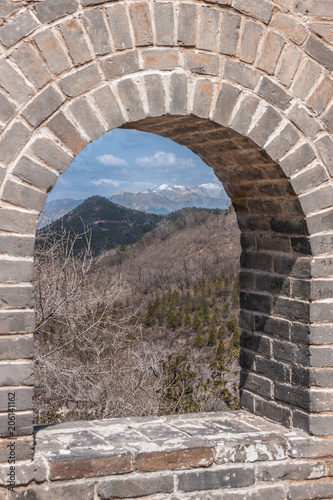 Beijing  China - April 28  2010  Great Wall of China at Badaling. Window in the wall shows gray-green wilderness and mountains with snow tops on horizon under blue sky.