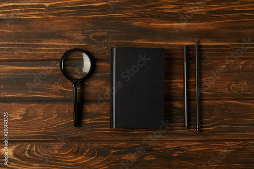 top view of magnifying glass, notebook and office supplies on wooden table