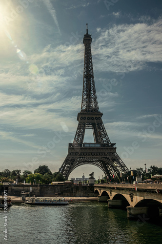 Tourist boat on Seine River, bridge and Eiffel Tower in a sunshine sky at Paris. Known as the “City of Light”, is one of the most impressive world’s cultural center. Northern France. Retouched photo.