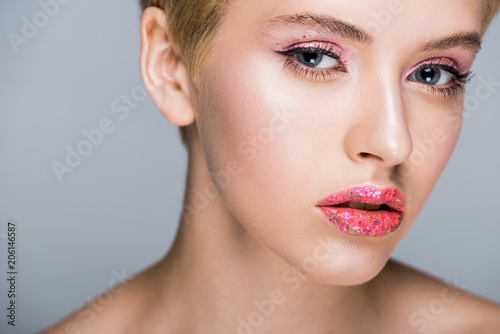 beautiful woman with stylish glittering makeup looking at camera isolated on grey