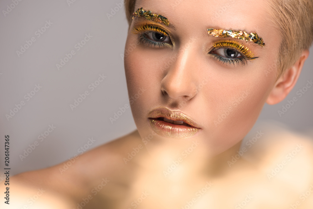 beautiful woman with golden bright glitter on face looking at camera isolated on grey
