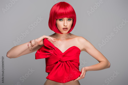 attractive woman with red hair and red top looking at camera isolated on grey