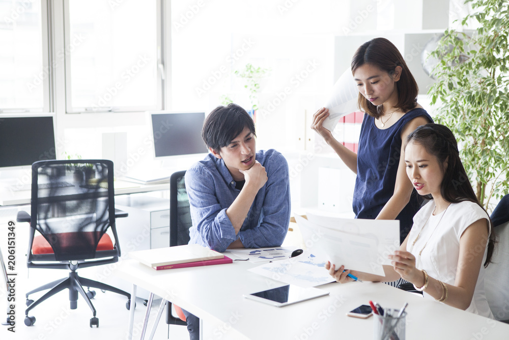 三人の会社員たちは資料見ながら会議をしている 三人の会社員たちは資料見ながら会議をしている