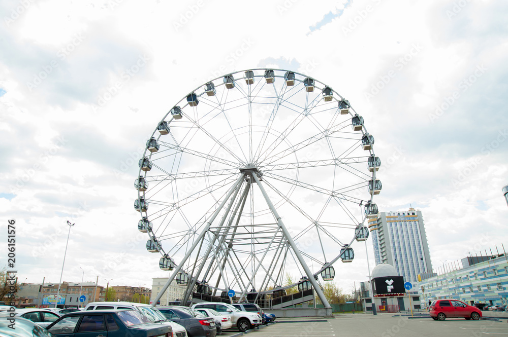 White fluffy clouds in deep blue sky, big Ferris wheel on sky background