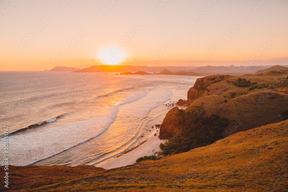 Tropical beach with rocks and ocean with waves at sunset