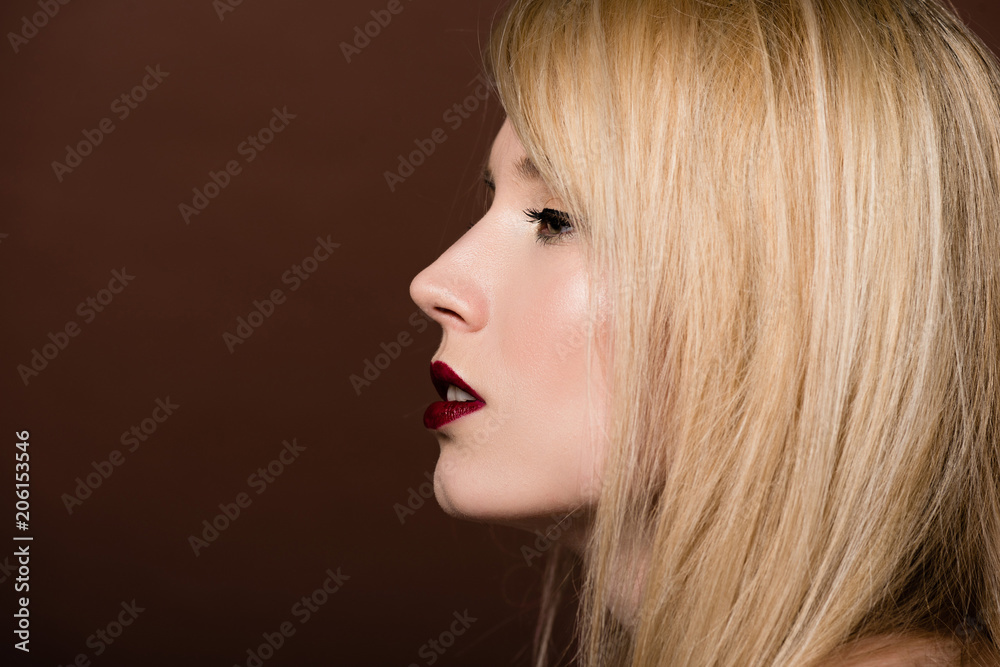 side view of beautiful young blonde woman looking away isolated on brown side view of beautiful young blonde woman looking away isolated on brown