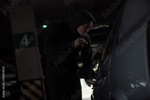 side view of focused male thief intruding car by picklock