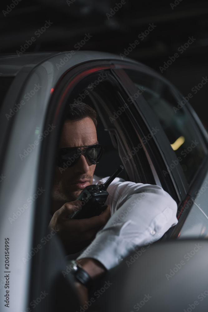 male undercover agent in sunglasses doing surveillance and using talkie  walkie in car Stock Photo