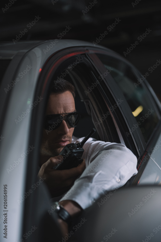 male undercover agent in sunglasses doing surveillance and using talkie walkie in car male undercover agent in sunglasses doing surveillance and using talkie walkie in car