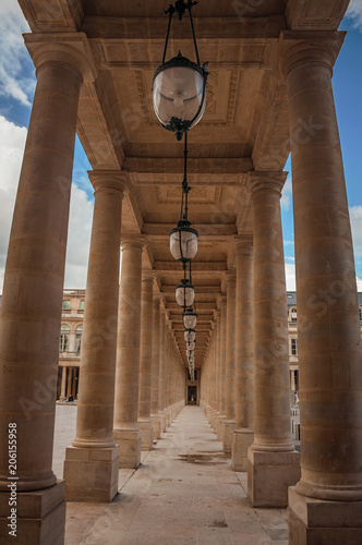 Photographie Sentier avec colonnade de marbre entre cours et ciel nuageux au Palais-Royal à Paris