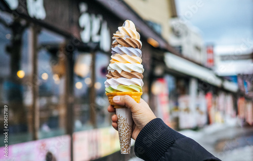 A women hand holding mixed colorful tasty ice cream soft cream cone with blurred shop background (selective focus)