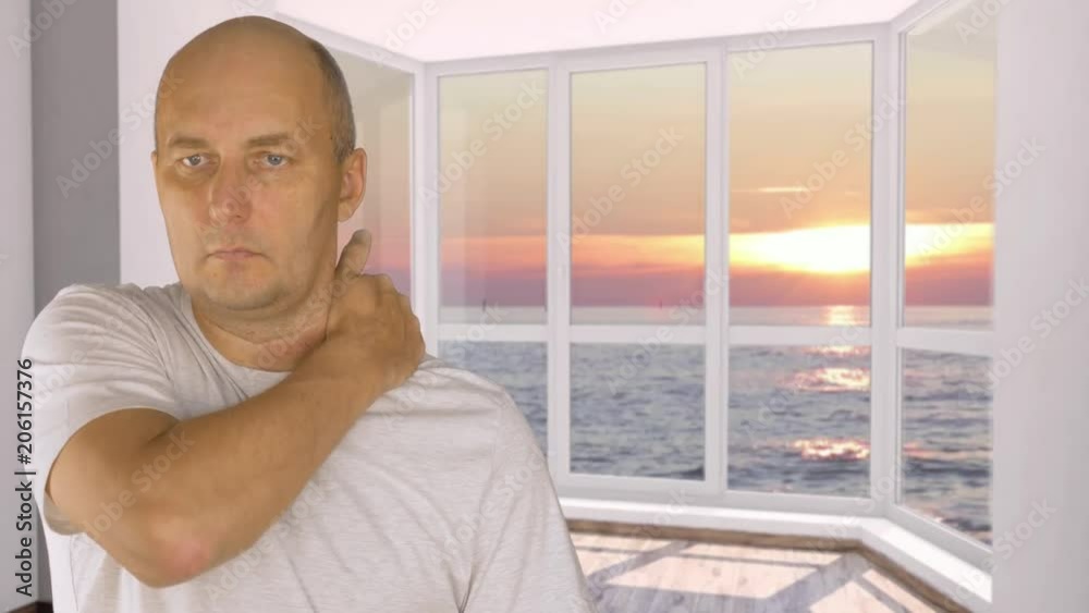 Man on background window with view on evening sunset doing himself shoulder massage Man on background window with view on evening sunset doing himself shoulder massage