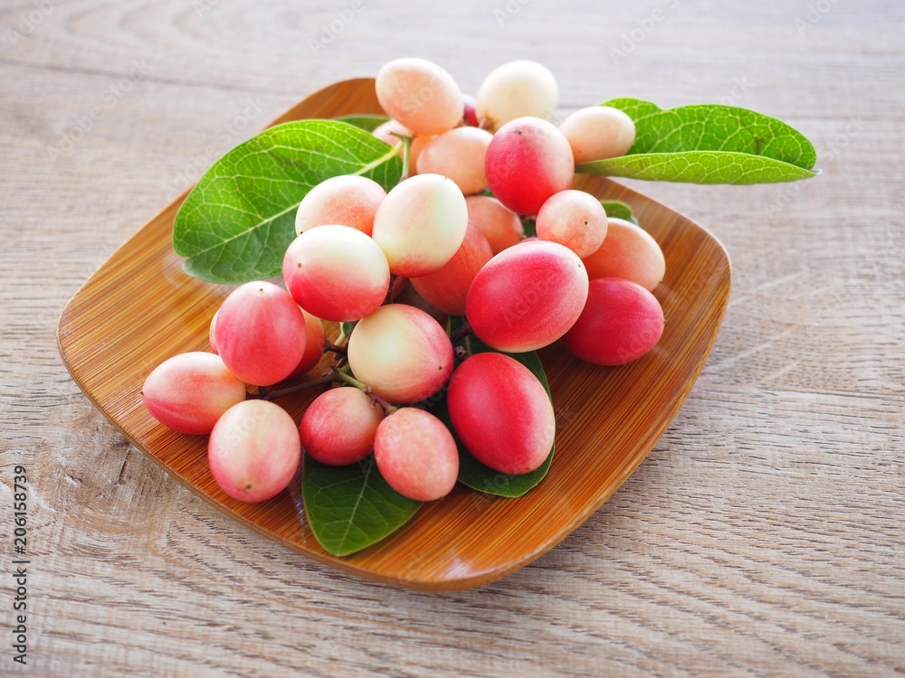 Carissa carandas or karonda are white and red with green leaves in wooden plates. On the old wood table It is a small fruit and has medicinal properties. Vitamin C is high when cooked to sour taste.