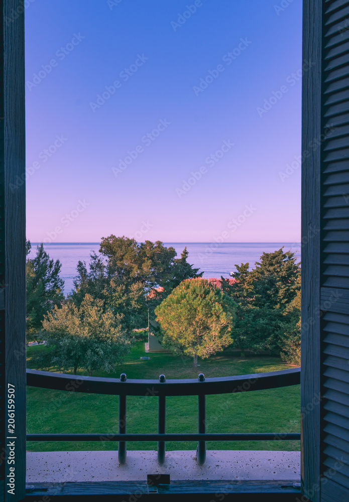 Fototapeta Piękny wschód słońca z otwartego okna z niebieskimi drewnianymi okiennicami, widok na Morze Adriatyckie i dom w stylu śródziemnomorskim w Chorwacji