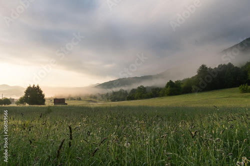 Misty mountains  early hazy morning over a mountain meadow or a field with green forested hills  Krasno polje village near Velebit mountain national park in Croatia