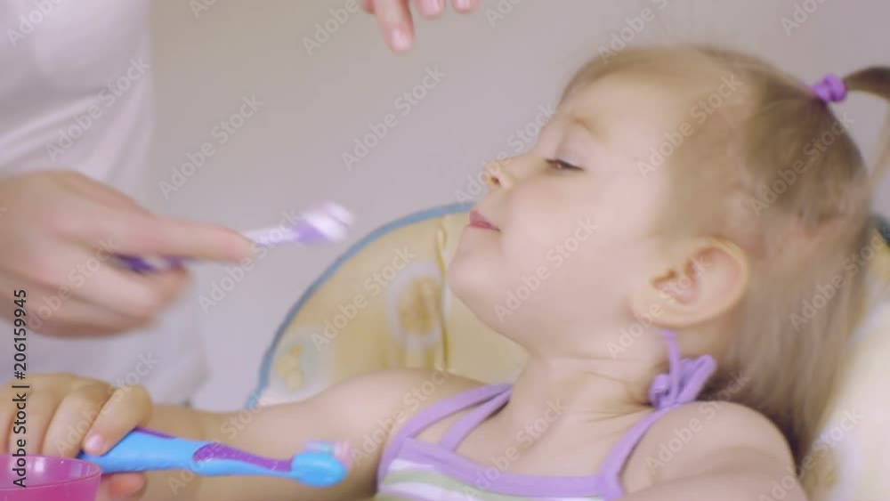 Close-up Mom helps to clean the teeth of her little daughter in the morning. Hygiene of the oral cavity. Care of teeth Close-up Mom helps to clean the teeth of her little daughter in the morning. Hygiene of the oral cavity. Care of teeth