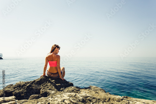 Woman sit on a rock beside the  calm sea. Travel and relax.