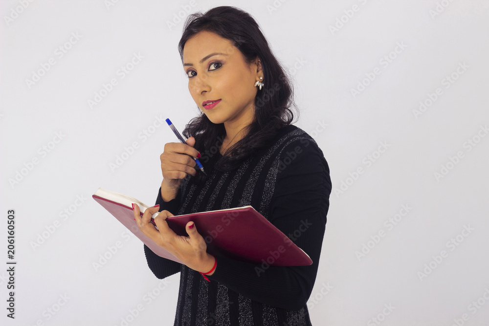 Smiling woman in black attire holding a book and pen and looking at camera. Front pose Smiling woman in black attire holding a book and pen and looking at camera. Front pose