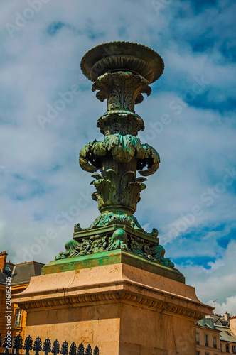Bronze decoration on marble pedestal with cloudy sky in Paris. Known as the “City of Light”, is one of the most impressive world’s cultural center. Northern France. Retouched photo.
