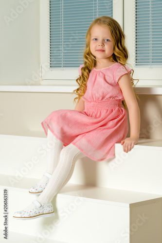 Beautiful little girl is sitting on the white staircase. © lotosfoto