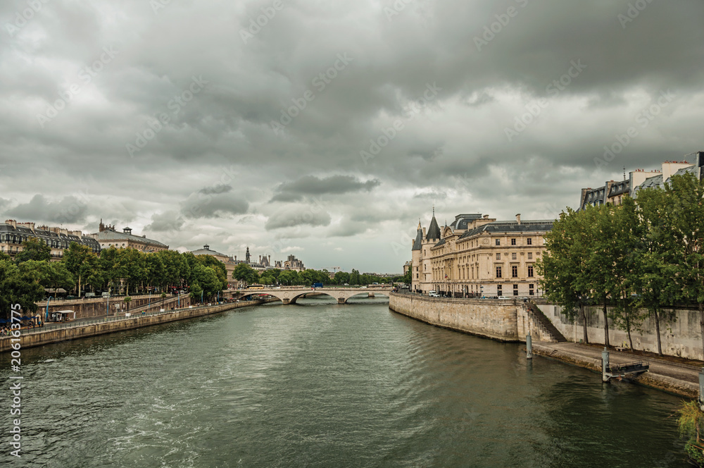 Old buildings, promenade with lined trees on the bank of Seine River and cloudy sky in Paris. Known as the “City of Light”, is one of the most impressive world’s cultural center. Northern France.