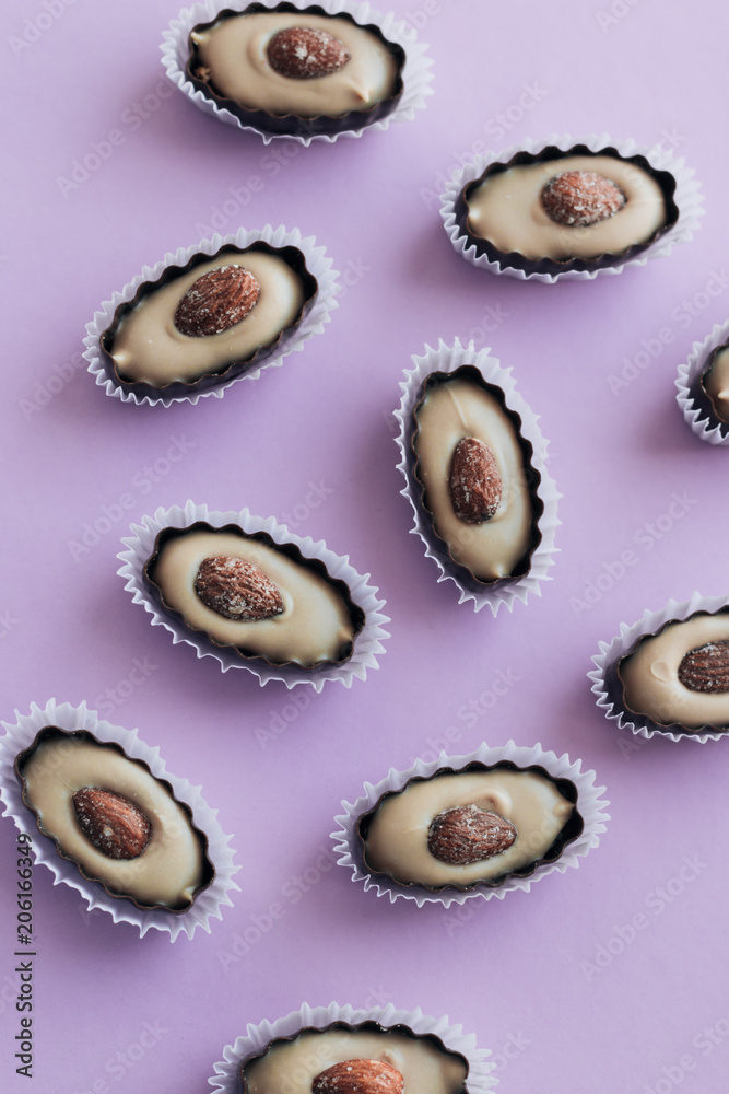 Flat lay of delicious praline sweets with almonds on purple background Flat lay of delicious praline sweets with almonds on purple background