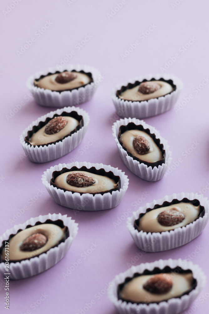 Flat lay of delicious praline sweets with almonds on purple background Flat lay of delicious praline sweets with almonds on purple background
