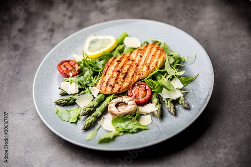 Grilled chicken breast asparagus arugula mushrooms tomatoes lemon and parmesan cheese.