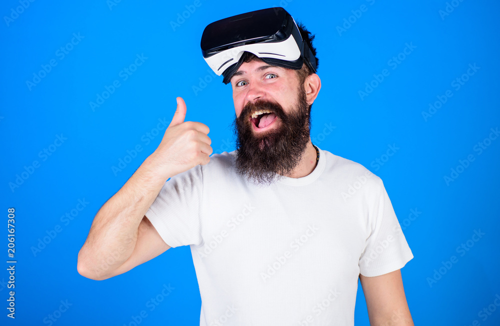 Man with beard and mustache with VR glasses, blue background. VR technology concept. Hipster on happy face shows thumbs up gesture. Guy with VR glasses or head mounted display Man with beard and mustache with VR glasses, blue background. VR technology concept. Hipster on happy face shows thumbs up gesture. Guy with VR glasses or head mounted display