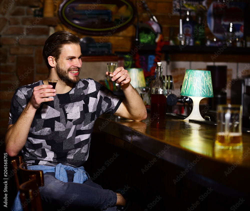 Guy at bar counter holds glasses of shot and rum.