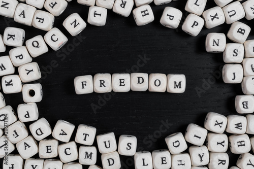 Word FREDOM on wooden cubes on a black wooden table with copy space