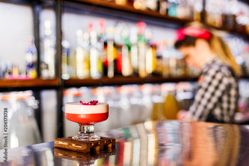 A lifestyle photo of a clover club alcoholic drink in a cocktail glass, served on a small wooden board, standing on a steel barstand. Selective focus, grain effect, bokeh background.