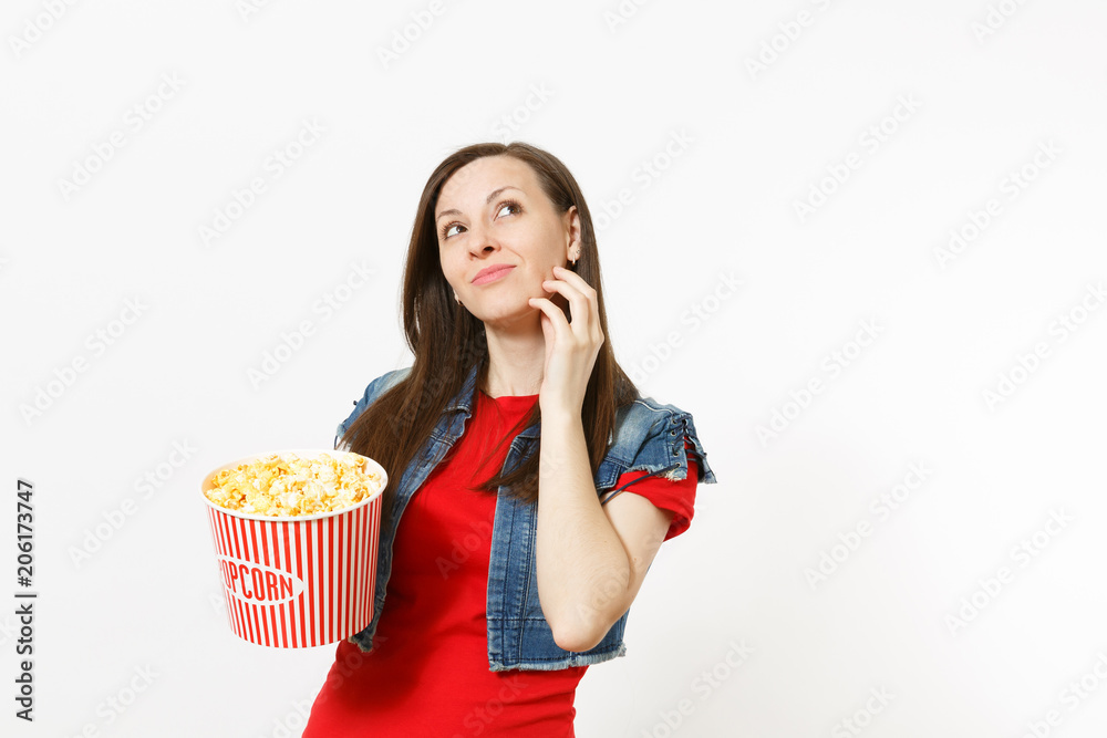Portrait of young pensive beautiful woman in casual clothes watching movie film, holding bucket of popcorn, looking up, keeping hand near chin isolated on white background. Emotions in cinema concept. Portrait of young pensive beautiful woman in casual clothes watching movie film, holding bucket of popcorn, looking up, keeping hand near chin isolated on white background. Emotions in cinema concept.