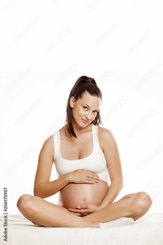 young pregnant woman sitting on a bed in the lotus position on a white background young pregnant woman sitting on a bed in the lotus position on a white background