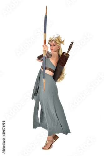 full length portrait of pretty blonde lady wearing fantasy toga gown, and holding a bow and arrow. standing pose on white background.
