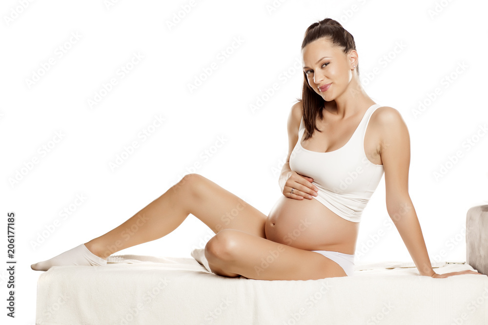 young pregnant pretty woman sitting on a bed on a white background young pregnant pretty woman sitting on a bed on a white background