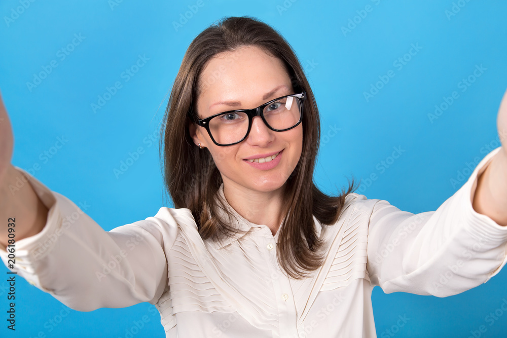 Young woman in glasses makes a selfie portrait on a blue background. Young woman in glasses makes a selfie portrait on a blue background.