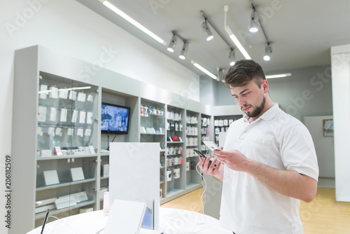 Wallpaper Mural Handsome bearded man is in the electronics store in the phone department and chooses a smartphone. Buyer buys a smartphone in a technology store. Purchase of a smartphone in a store. Torontodigital.ca