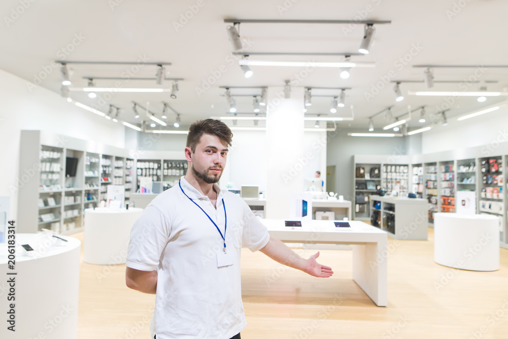 Portrait of a consultant who stands at the entrance and invites you to the technology store. Conlutant stands on the background of a modern light electronics store