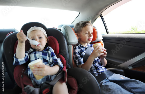 Obraz na płótnie Little sister and her brother in safety car seat eating sweet ice cream. The little girl is capricious w salonie