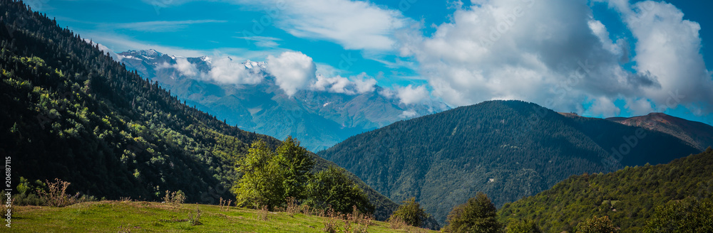 Amazing panoramic view to Caucasus Mountains. Densely coniferous forests and high snowed mountain peaks. Sunny day with blue mountains. Svaneti, Geogria.