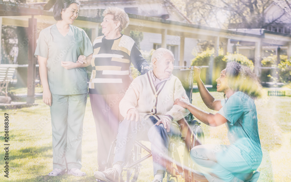 Double exposure of asian and african nurses helping elder couple at rehab facility garden