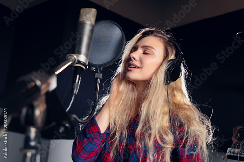Music expresses you  Side view portrait of the young woman singer with headphones recording a song in front of the microphone.