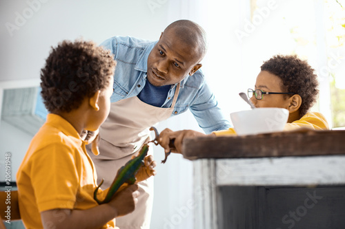 Keep calm. Caring young father asking his sons to behave themselves while they playing with toy dinosaurs too loudly during breakfast photo