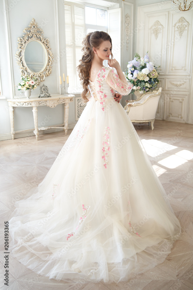 An elegant woman in a long light dress with embroidery in a chic interior.